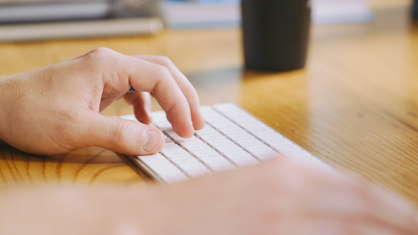 Hands typing on a white keyboard on a wooden desk.