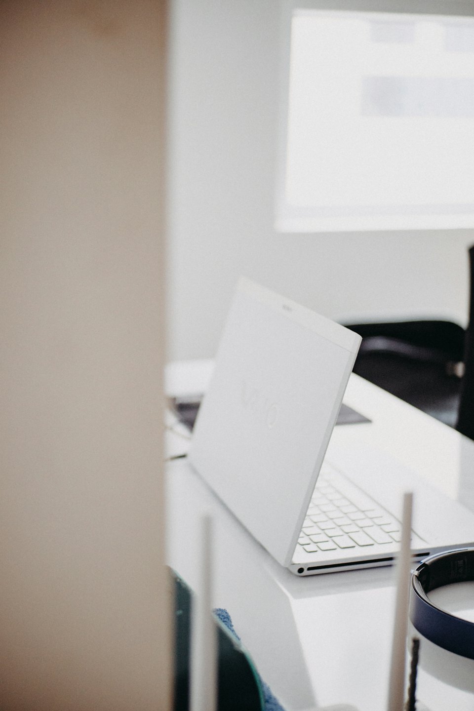 Open laptop and blue headphones sitting on a white desk.